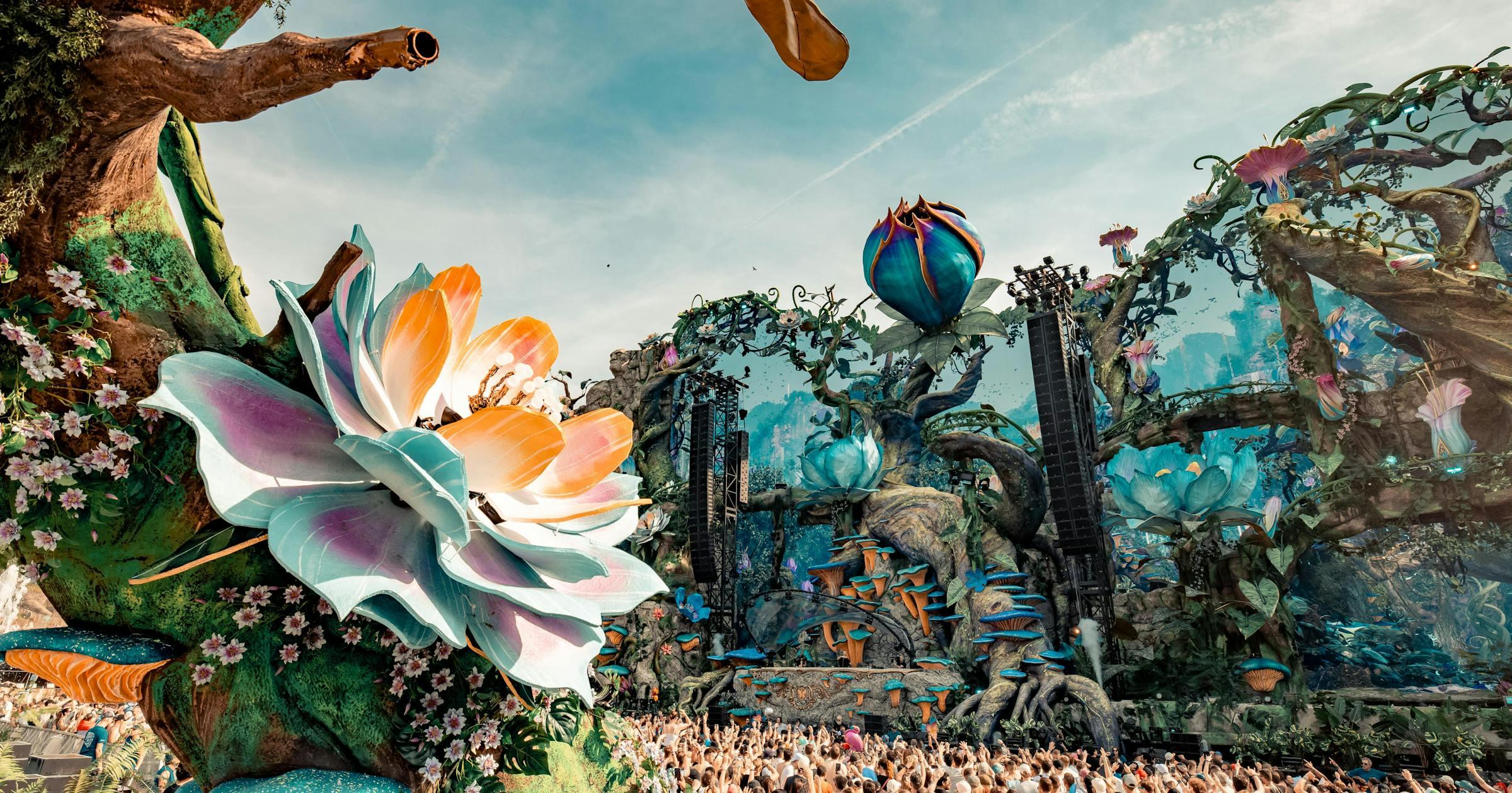 Tomorrowland Brasil main stage with vibrant floral decor, lush trees, and a huge crowd.