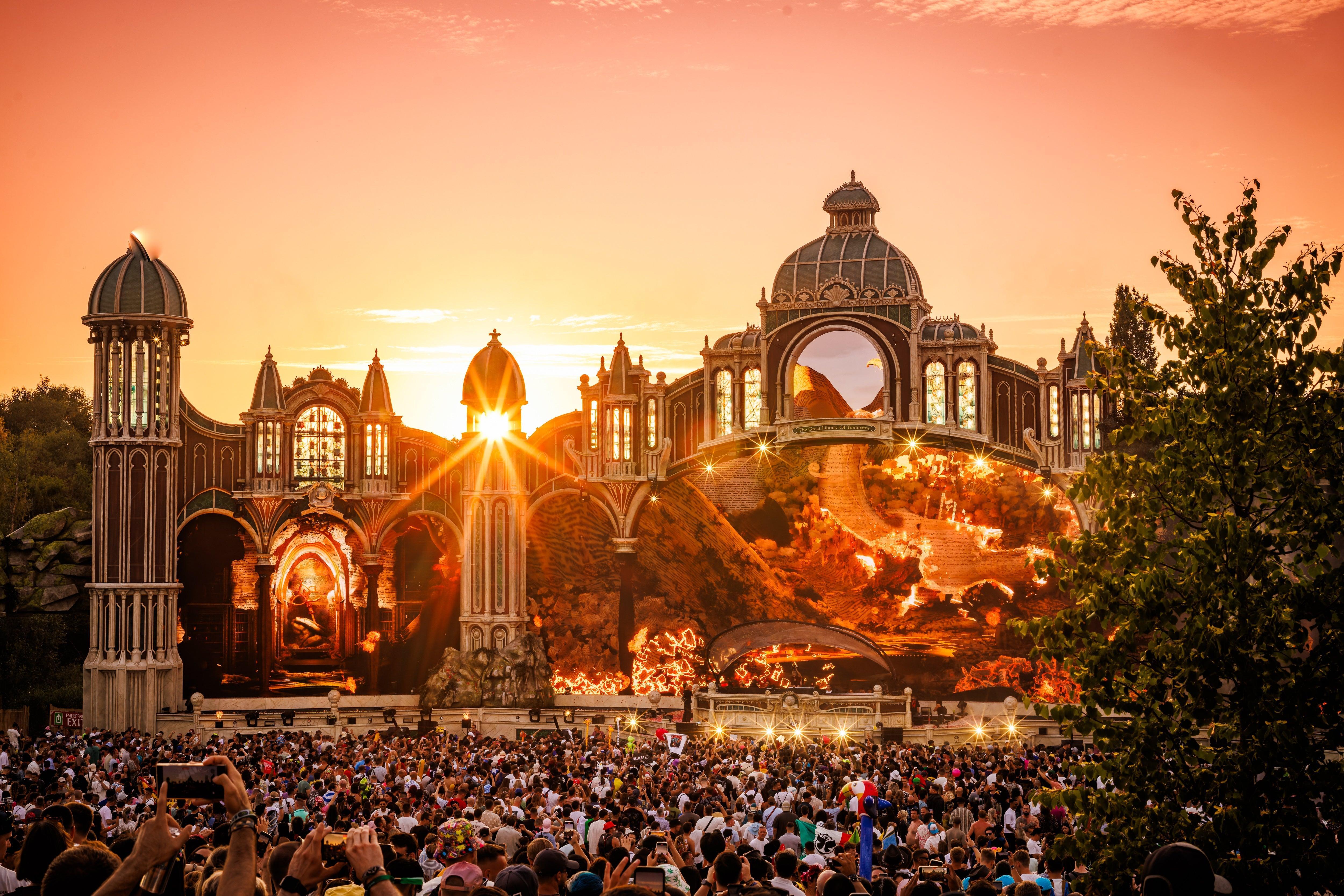 Tomorrowland main stage at sunset, with a large crowd and vibrant orange sky.