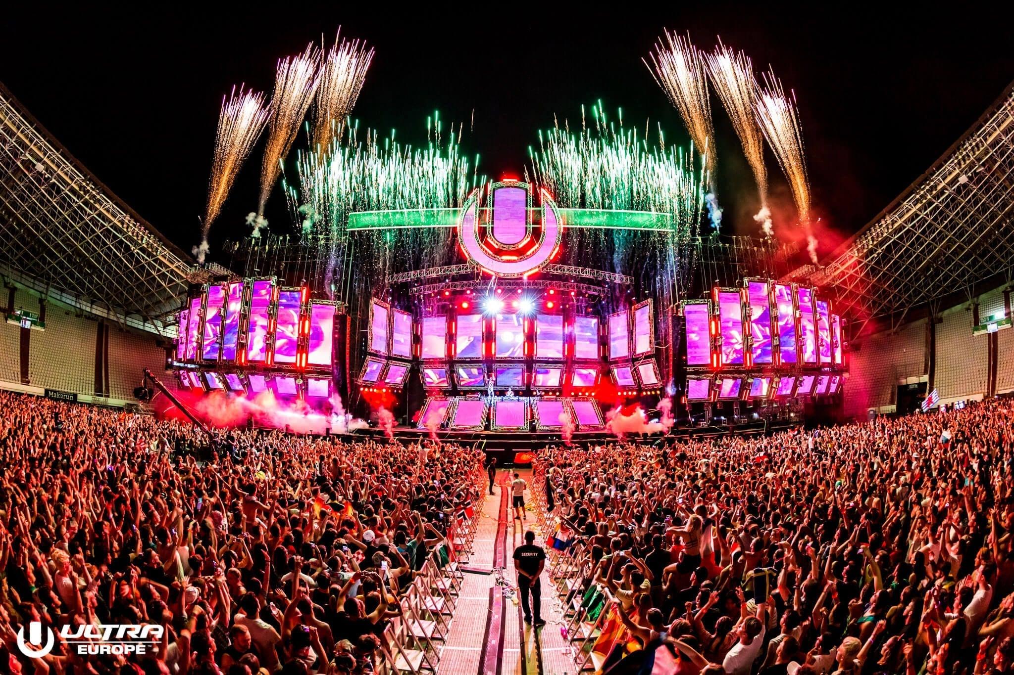 Massive crowd at Ultra Europe festival, fireworks exploding over a vibrant stage with LED screens.