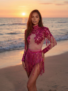 Body Alessia Rose in paillettes con gonna a frange, con collo alto e spalle strutturate, su una spiaggia al tramonto.