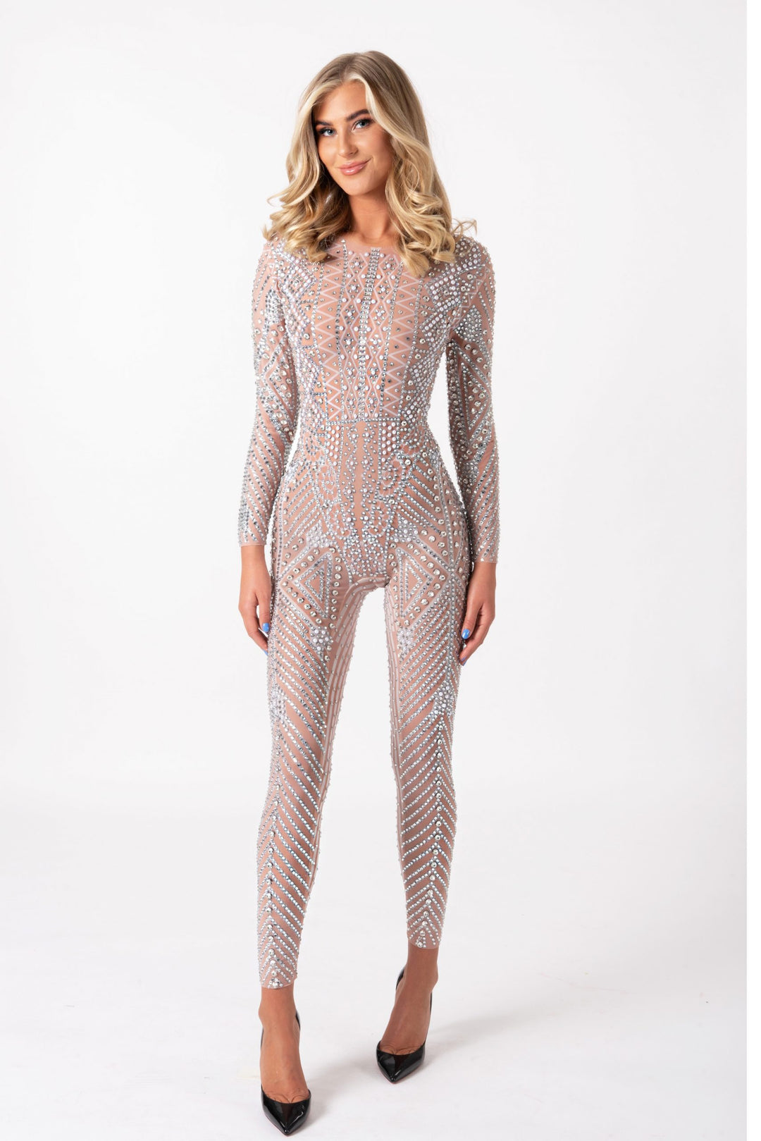 Model wearing a long-sleeve, nude-toned jumpsuit covered in intricate, hand-glued silver rhinestones in a geometric pattern.