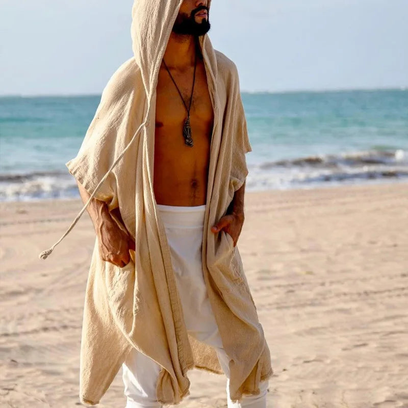 Men's sand polyester hooded cape with wide bat-wing sleeves and pockets, worn on a beach.