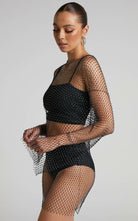 Modelo vistiendo un vestido negro de red con diamantes de strass, mostrando un diseño transparente y detalles brillantes.