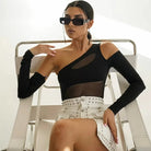 Zwart mesh bodysuit gedragen door een model met een zonnebril, gestyled met een witte versierde rok.