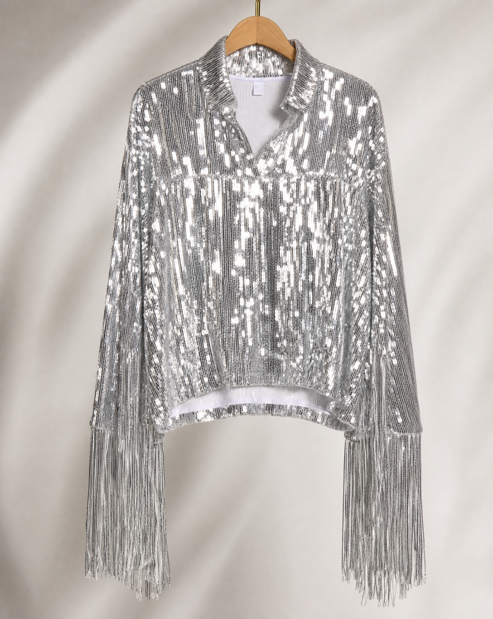 Silver sequin jacket with long fringe sleeves, displayed on a wooden hanger.
