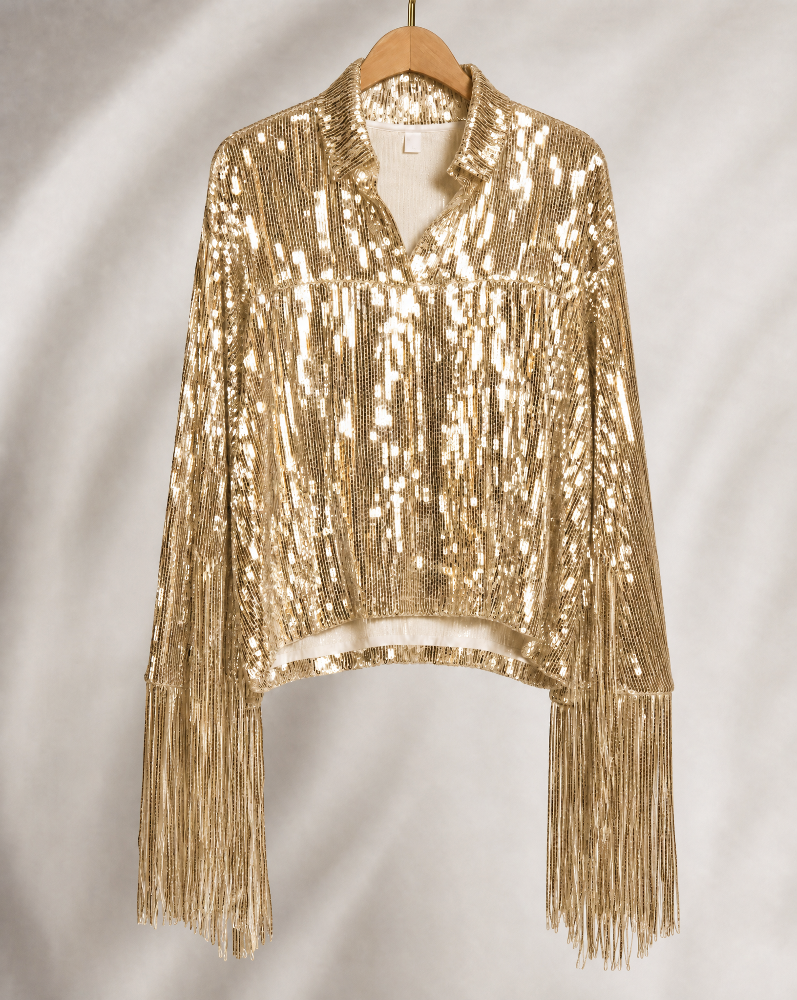 Gold sequin fringe jacket with long sleeves, hanging on a wooden hanger.