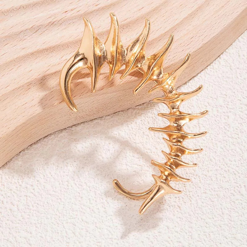 Gold cyberpunk ear cuff with sharp angular spikes in a biomechanical spine design, no piercing required.