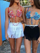 Due donne che indossano outfit colorati con frange e decorazioni di gemme, mostrando la moda da festival.