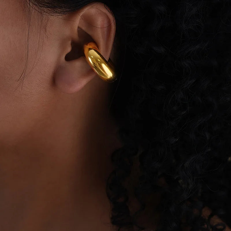 Shiny gold-toned metal ear cuff, thick and smooth, worn on a person's ear.