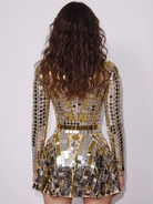Back view of a woman in a dazzling gold sequin mini dress with long sleeves and a fitted waist.