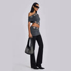 Mannequin portant un ensemble deux pièces composé d'un crop top épaules dénudées et d'une mini-jupe, avec un pantalon noir élégant et des lunettes de soleil.