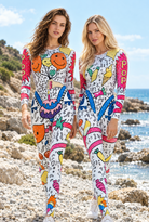 Two models wearing long-sleeve, rhinestone-embellished jumpsuits with colorful pop-art prints on a rocky beach.