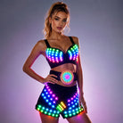 Model wearing a black LED light-up rave bra, belt, and shorts set with multicolored glowing grid patterns.