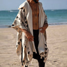 Men's Tulum Fringe Cardigan: beige polyester with black geometric patterns and fringe hem, worn open on a beach.
