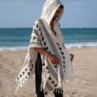 Men's Tulum Fringe Cardigan in cream polyester with black geometric patterns and a hood, worn on a beach.