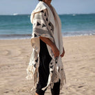 Men's Tulum Fringe Cardigan: cream polyester with black geometric print, hooded, open front, fringe hem, beach setting.