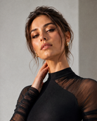 Model wearing a black mesh patchwork bodysuit with a high neckline and sheer long sleeves.