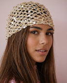 Cuffia beige in rete all'uncinetto con paillettes dorate indossata da un modello.