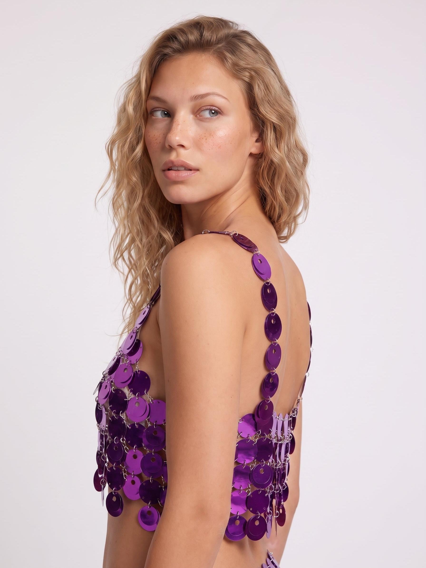 Model wearing a metallic purple chain link bra top constructed from reflective circular discs against a white background.
