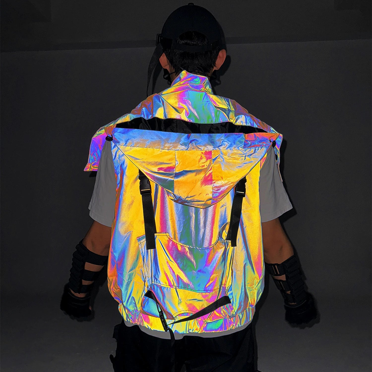 Multicolor reflective techno vest with a large hood and black strap details, worn by a person from behind.