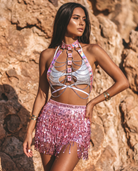 Model wearing a pink iridescent harness with metallic chains over a silver bikini top and a sequin fringe mini skirt.