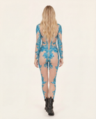 Blonde model from behind in a sheer sky blue rhinestone and sequin jumpsuit with black boots.