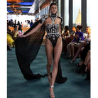 Modelo luciendo un body con pedrería y capa, con pedrería brillante y una capa fluida y dramática.