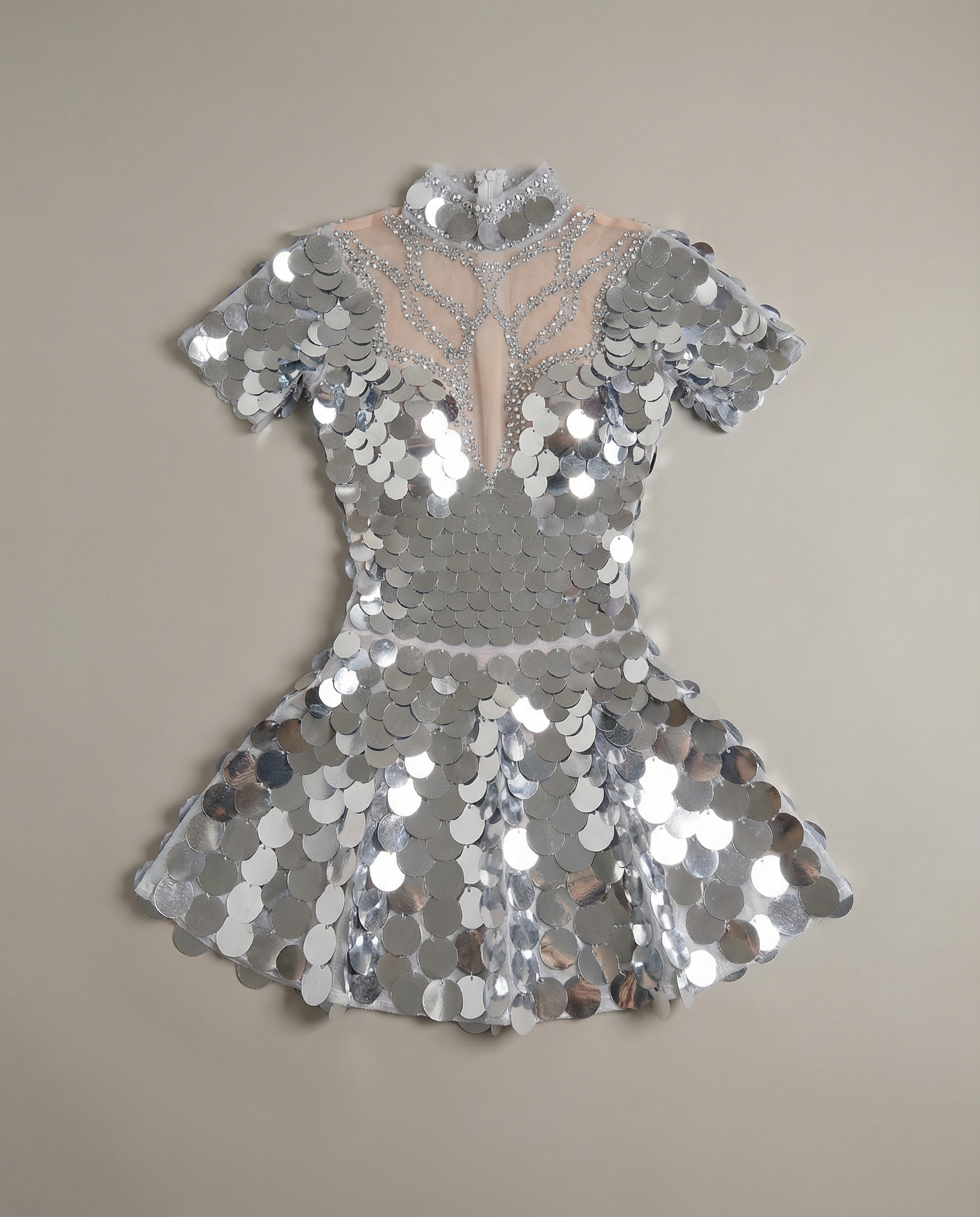 Vestido mini de lentejuelas plateado con espejo y pedrería, con escote de malla transparente y mangas cortas.