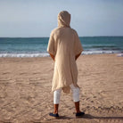 Men's sand polyester hooded cape with wide bat-wing sleeves, viewed from behind on a beach.