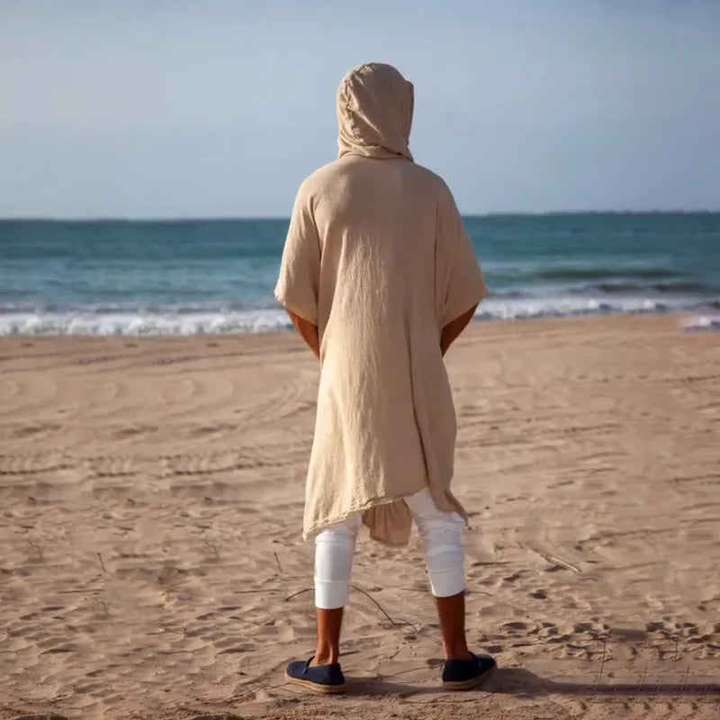 Men's sand polyester hooded cape with wide bat-wing sleeves, viewed from behind on a beach.