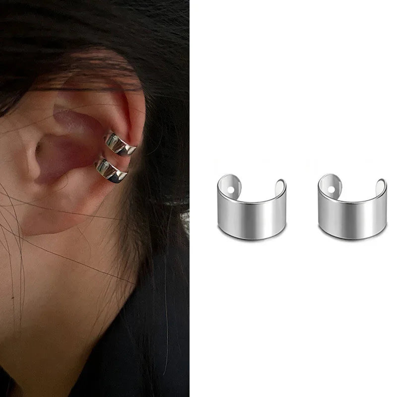 Silver metal ear cuffs, one shown worn on the ear, featuring a sleek, minimalist band design.