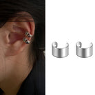 Orecchini a clip in metallo argento, uno indossato sull'orecchio, con un design a fascia elegante e minimalista.
