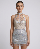 Model wearing a silver holographic chest harness with metallic chains over a sequin fringe mini skirt.