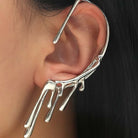 Polsino auricolare completo in metallo argento con design a liquido che gocciola e si scioglie, indossato sull'orecchio sinistro.