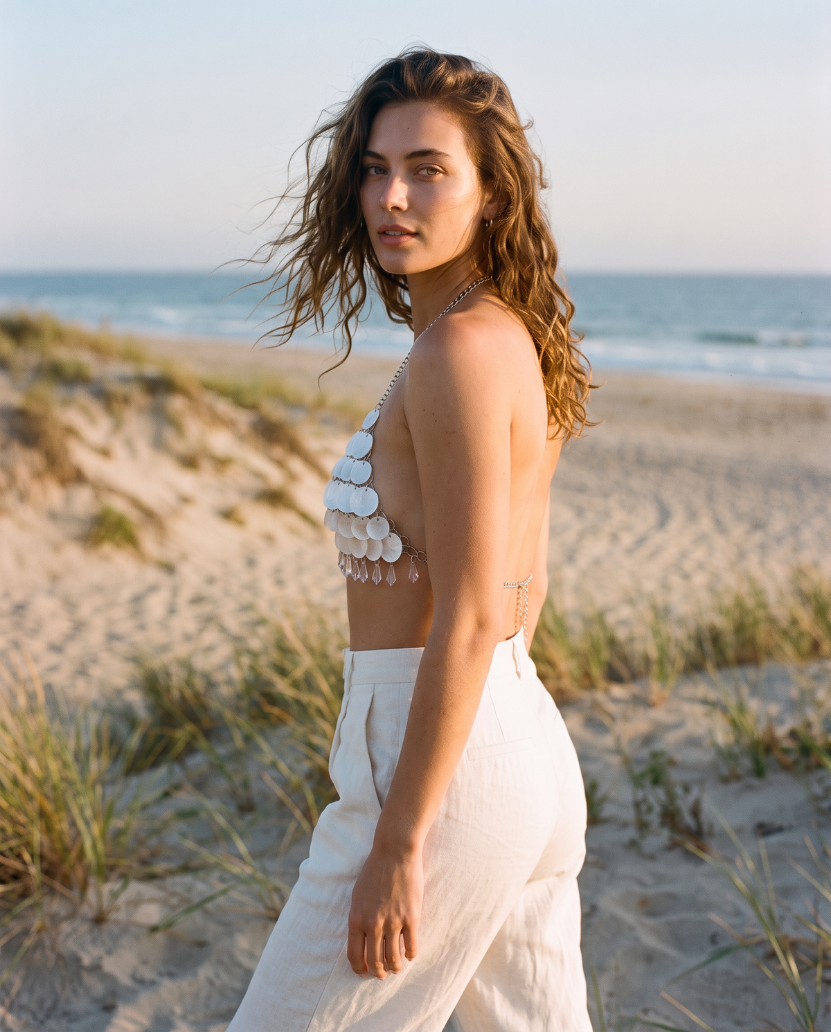 White seashell bra top featuring layered shell discs and delicate silver metal chains on a beach background.