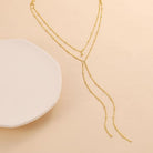 Collar Dorado de cadena que presenta dos finas cadenas curb con un elegante detalle colgante.